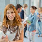 Girl holding laptop with group of students in college library