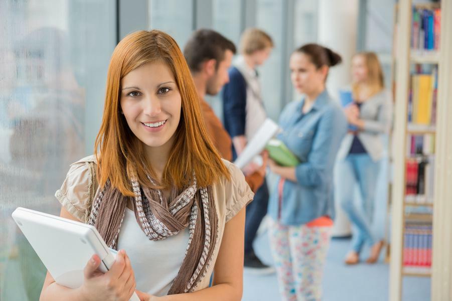 Girl holding laptop with group of students in college library
