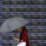 Mulher passa por painel de cotações em frente a Bolsa de Valores de Tóquio